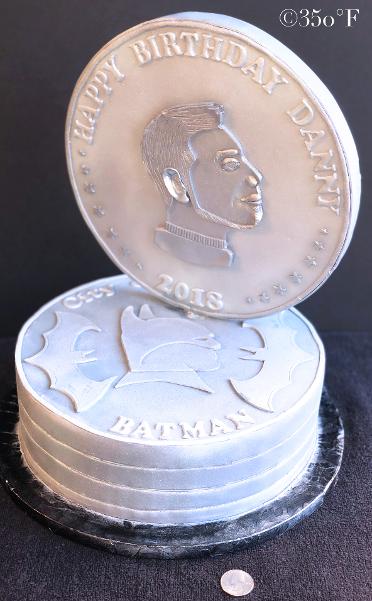 A batman themed cake created as a stack of Gotham City currency coins with a profile of Batman on one side and the profile of Danny on the other.