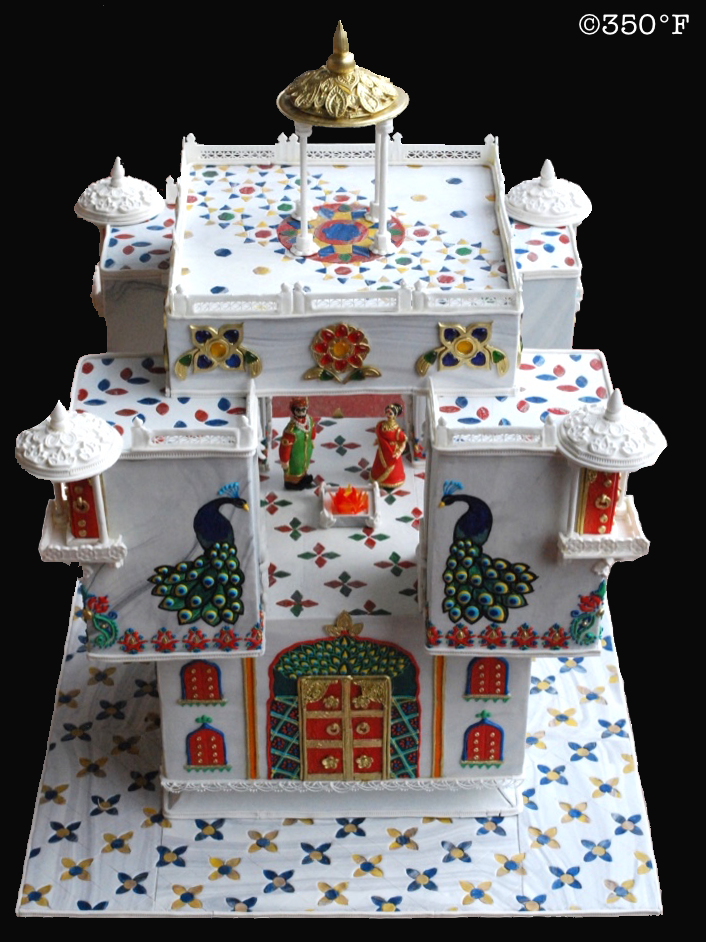 An ornate indian wedding cake with peacock and figurines of bride and groom.