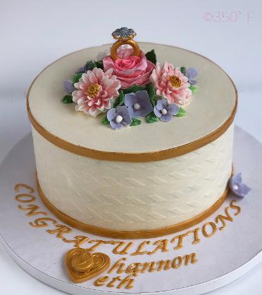 A buttercream engagement cake with fondant flowers and a beautiful edible ring cake topper