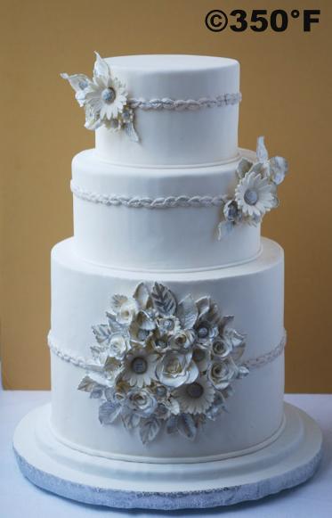 A white and silver wedding cake with a bunch of silver gilded flowers